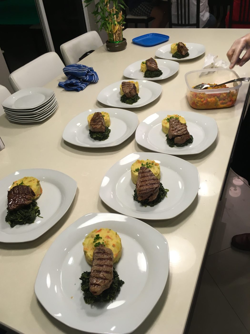 Plates of grilled steak with mashed potatoes and spinach lined up on a table, ready to serve